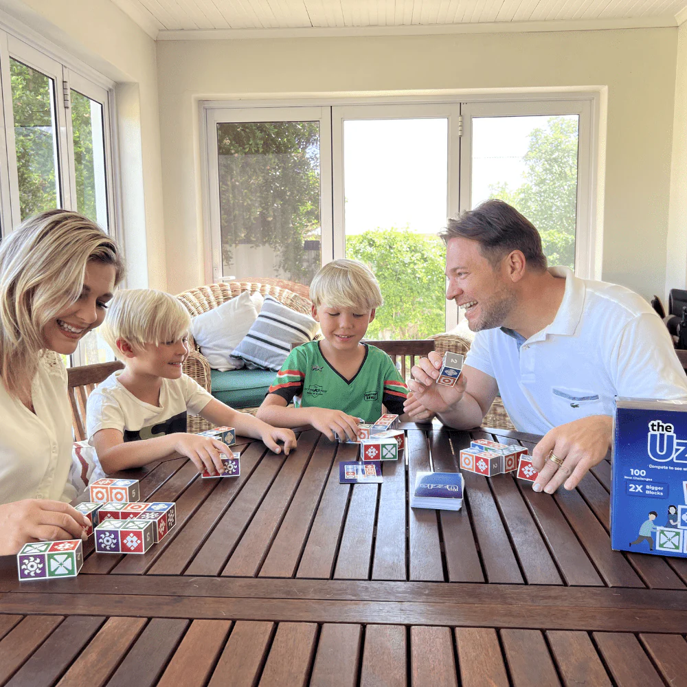Family playing a tabletop game with colorful blocks at a wooden table in a sunlit room.