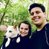 Couple smiling with a dog in a lush, green forest.