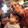 A woman playfully sticking out her tongue while holding a curious child in a store.